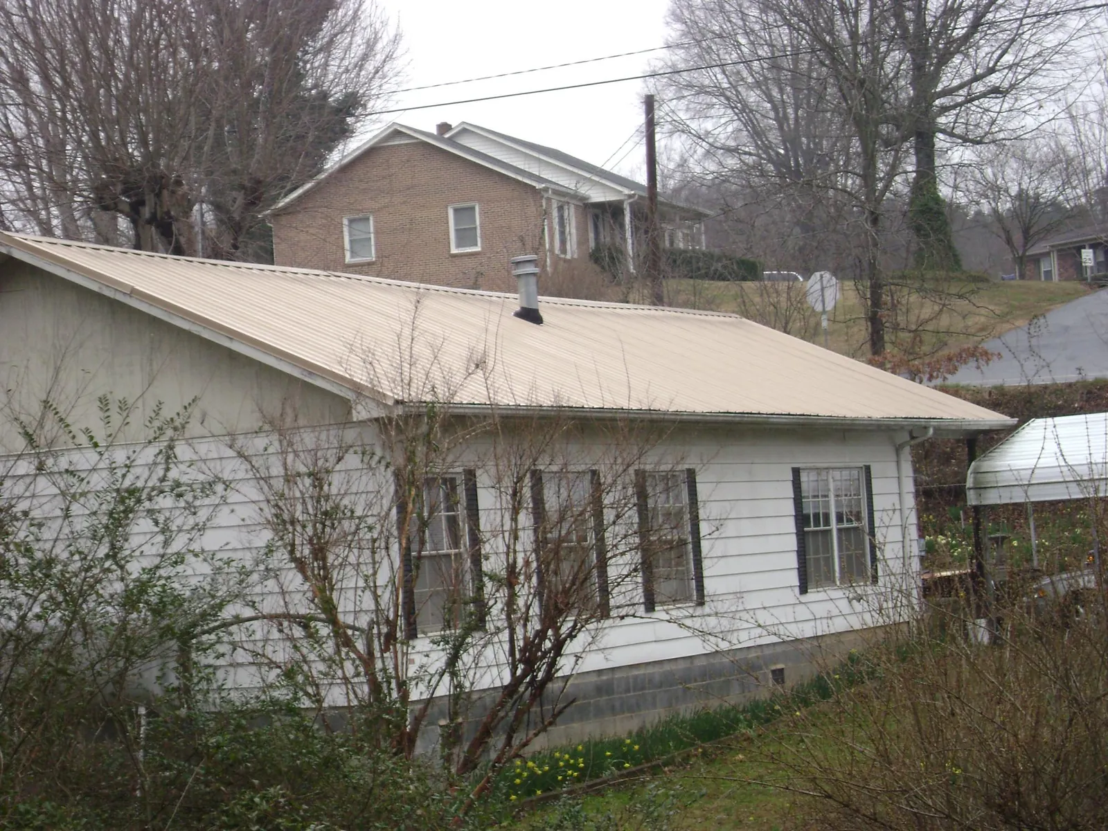 Tan metal roof on a white sided house set into a hillside — Commercial Roofing by Roofing Brothers in Point Pleasant Beach